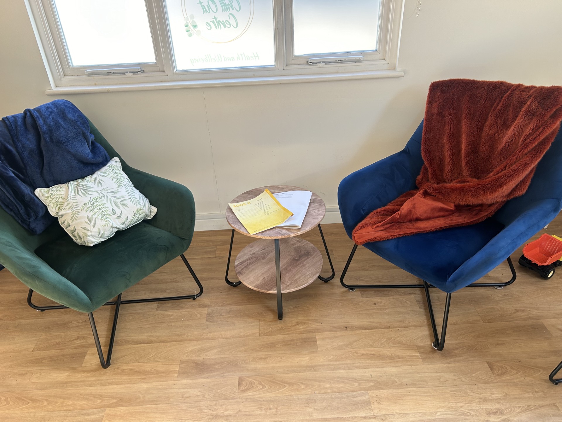 Two soft armchairs with blankets and cushions beside a small table in a calm, naturally lit room