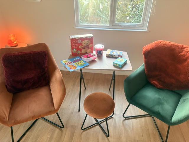 A small table set with picture books, puzzles and games between two soft armchairs, with a warm salt lamp nearby