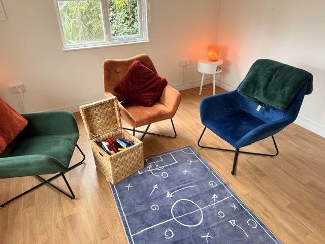 Assessment room with four soft armchairs, a basket of toys, a rug and warm lamp lighting